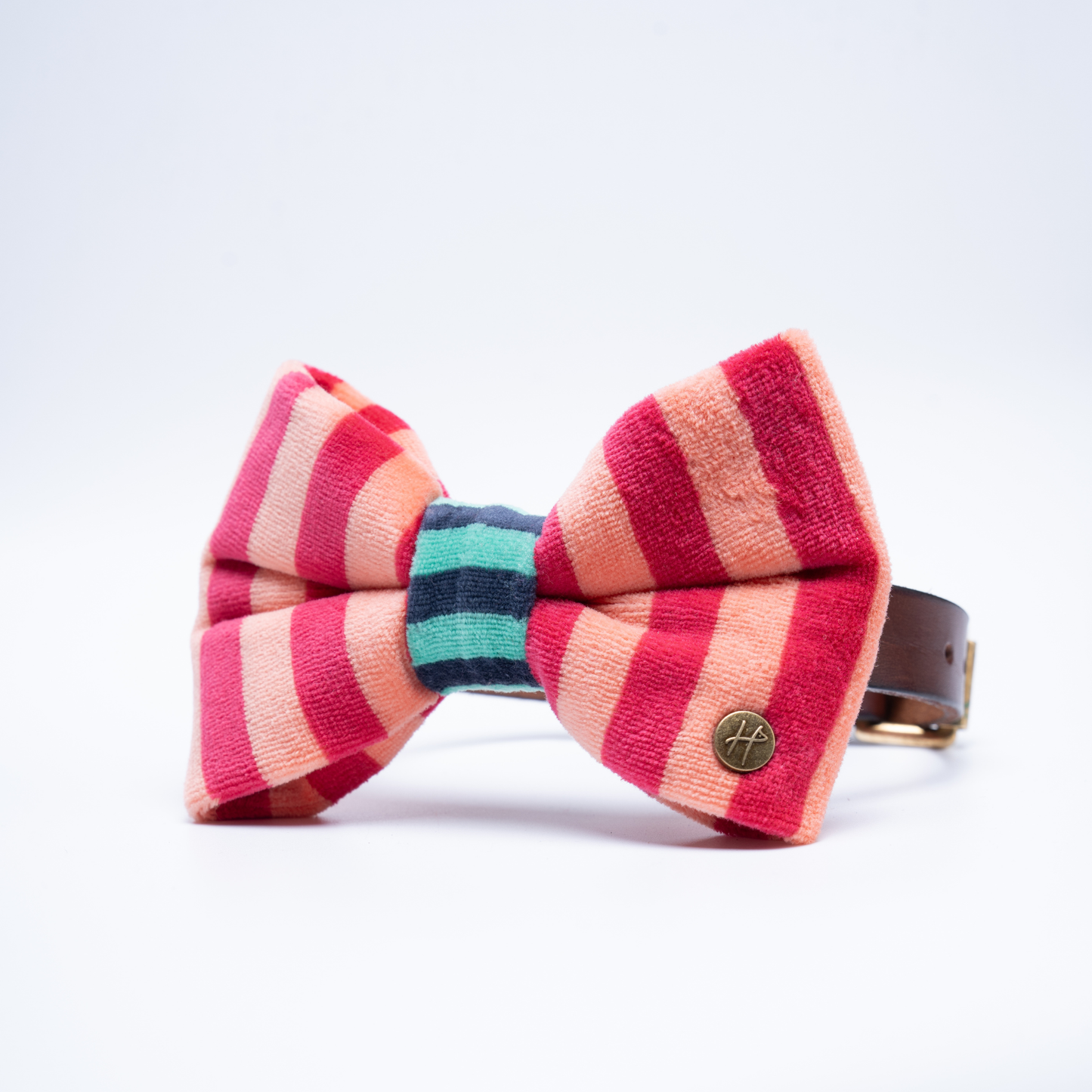 A striped bow tie made of textured fabric with alternating pink, coral, and peach vertical stripes, featuring a teal and navy striped centre band set against a clean white background.